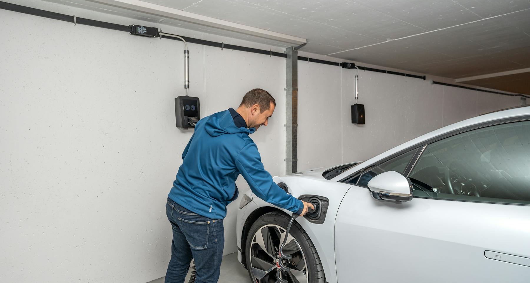 Conductor conectando un auto electrico en un garage residencial.